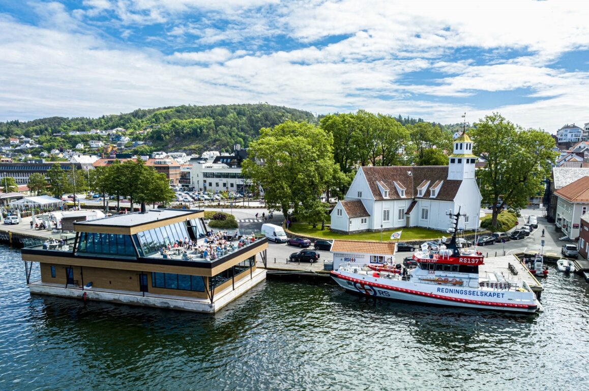 Drone shot featuring the sea, a boat, an outdoor restaurant, a rooftop terrace, and a church